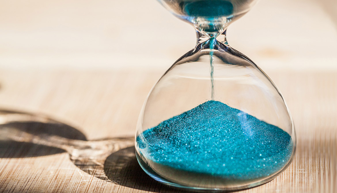 Blue sand running through the bulbs of an hourglass measuring the passing time in a countdown to a deadline