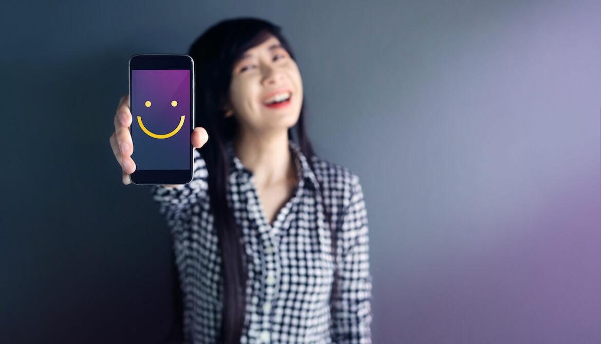 happy woman with smiley face on her cell phone screen showing her good experiences