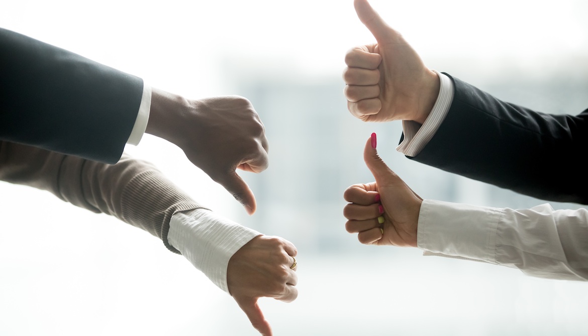 Hands of diverse business people showing two thumbs up and two thumbs down, suggesting equal opposing forces