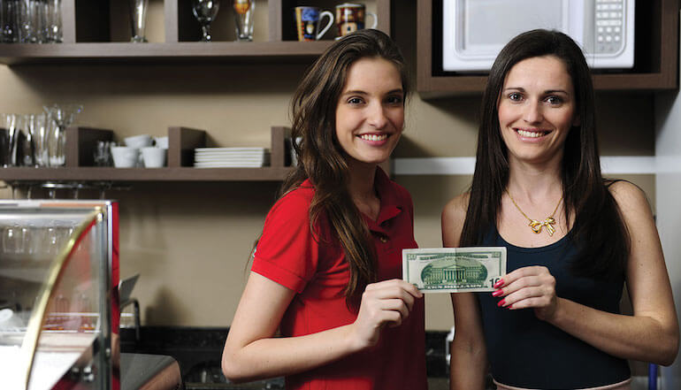 Two women each hold one corner of a dollar bill