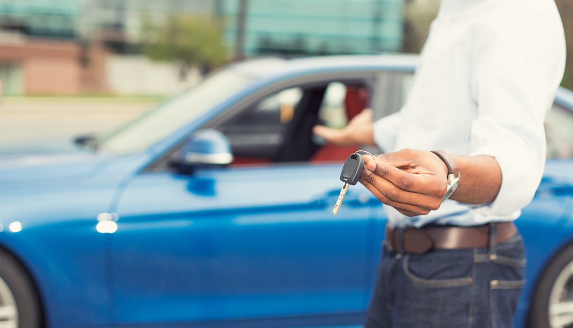 African American man holding out keys to a new blue car