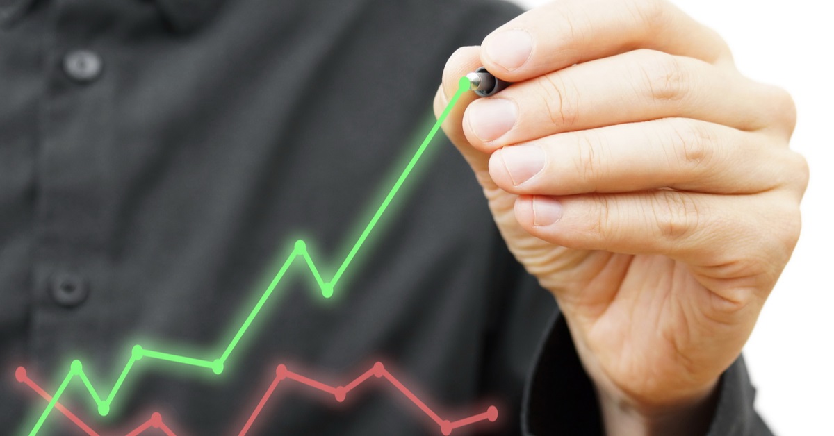 Man in black shirt drawing a green financial graph above an existing red financial graph