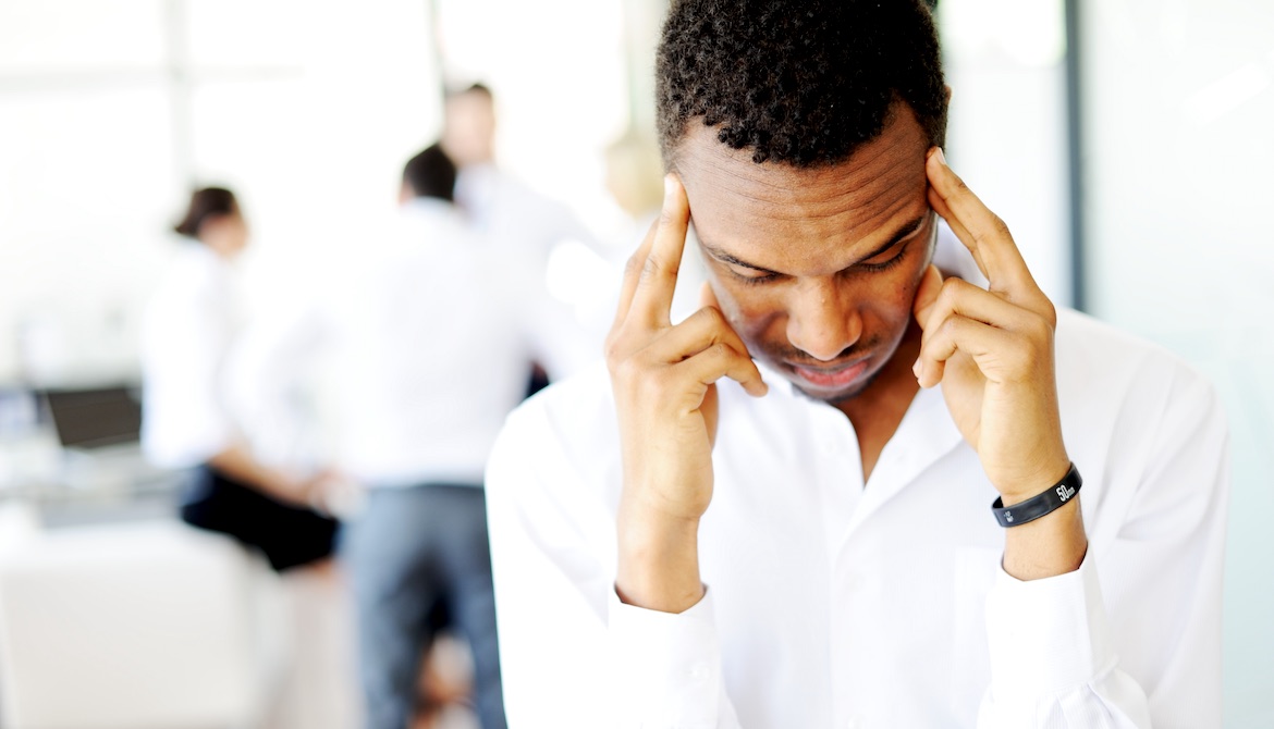 stressed new Black business leader rubs his temples while teammates talk in office background