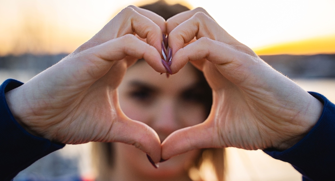 A young Gen Z woman creates a heart shape with her hands