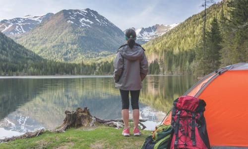 Woman at campsite looks over a lake to a distant mountain peak