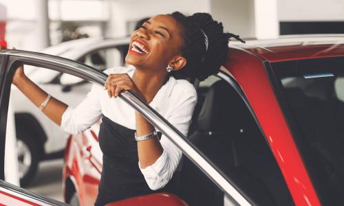 excited young African American woman smiles next to new red car