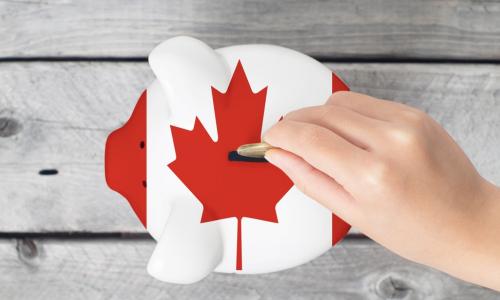hand dropping coin into piggy bank painted to look like Canadian flag
