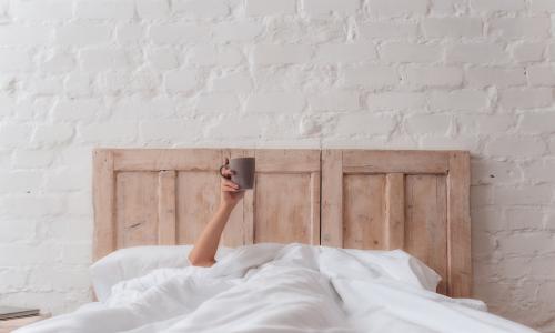 woman’s hand sticking out of white bed covers holding cup of coffee