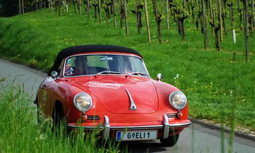 a vintage red Porsche drives along a country highway