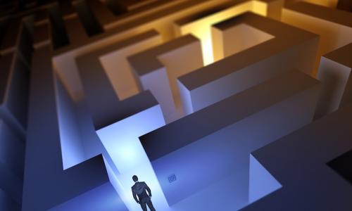 usinessman stands at entrance to maze with sections in both shadows and bright light