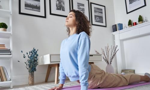young woman doing yoga in home office while watching online video class