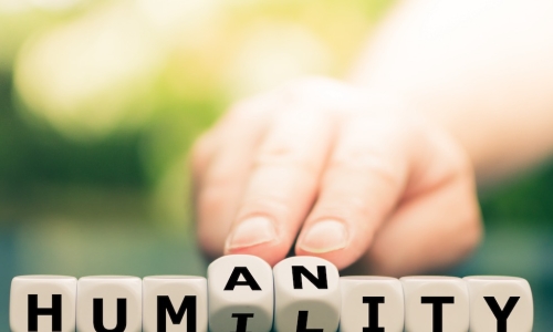 hand switching the middle letters of the word HUMANITY to HUMILITY