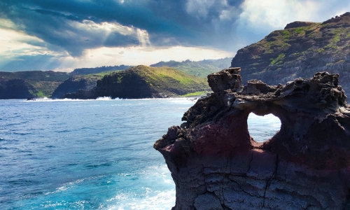 A hole in rocks in Maui forms a heart with ocean in background