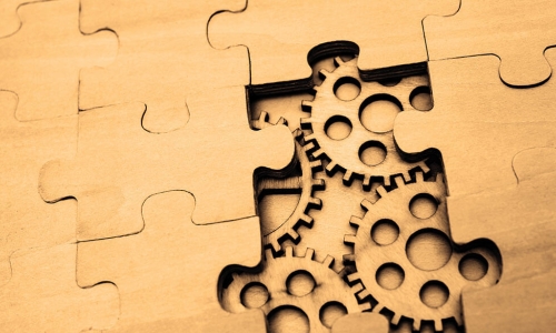 wooden puzzle pieces connected together with a pair of pieces missing to reveal gears and cogwheels