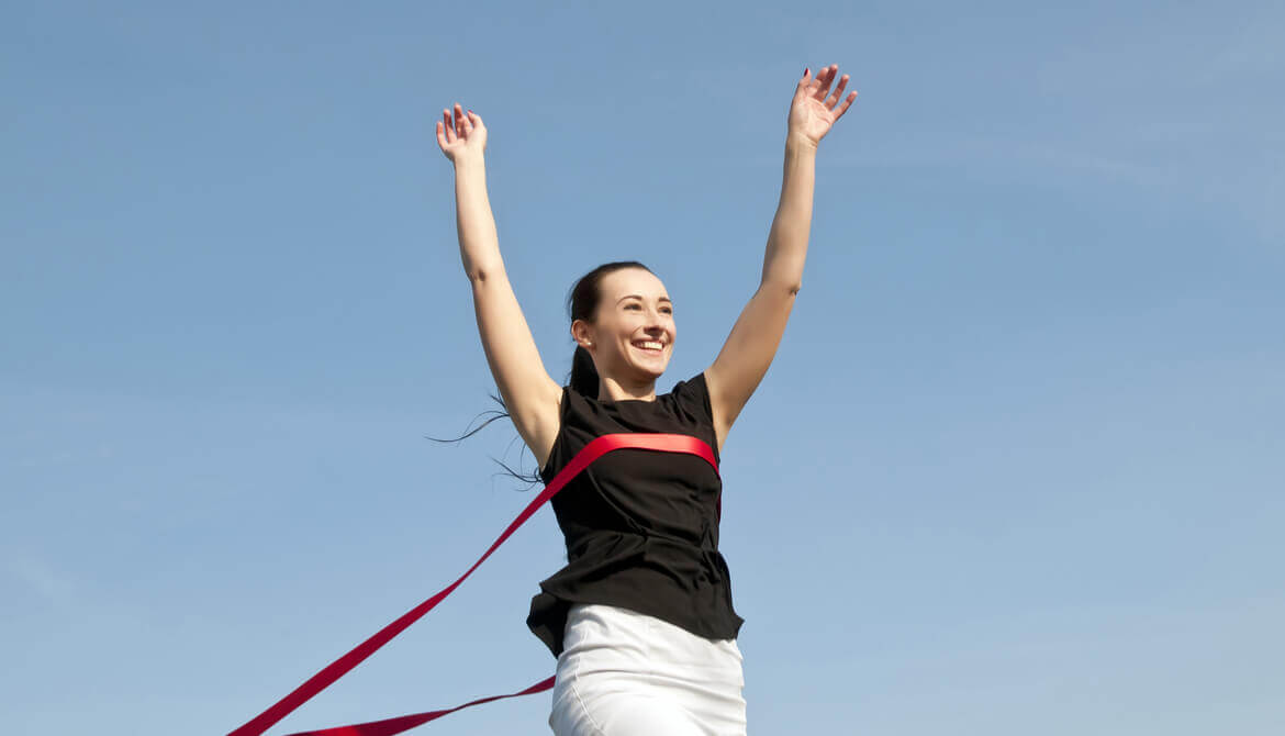 business woman breaks through tape at end of the race