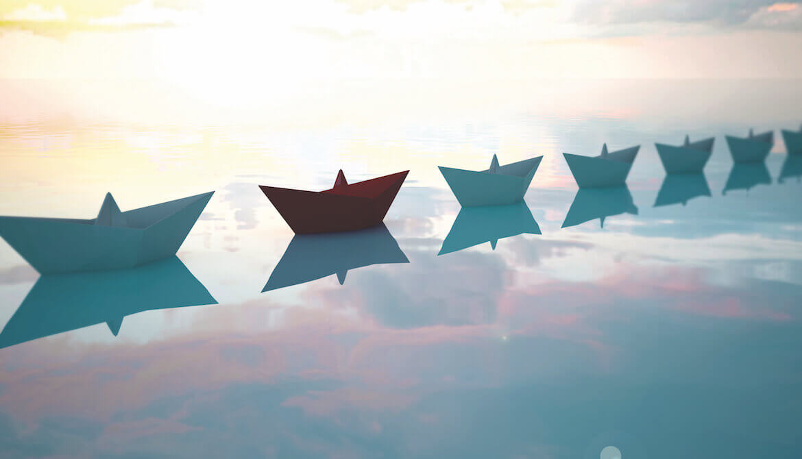 one red boat in a line of blue paper boats