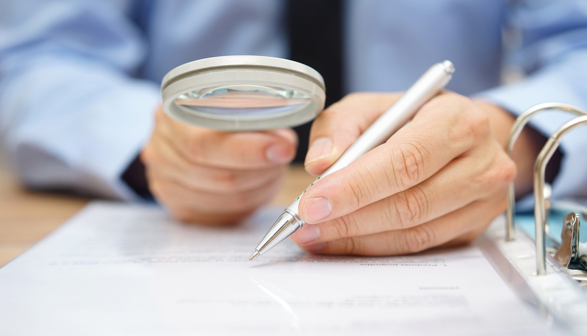 examiner reviewing paperwork in a binder through a magnifying glass representing due diligence