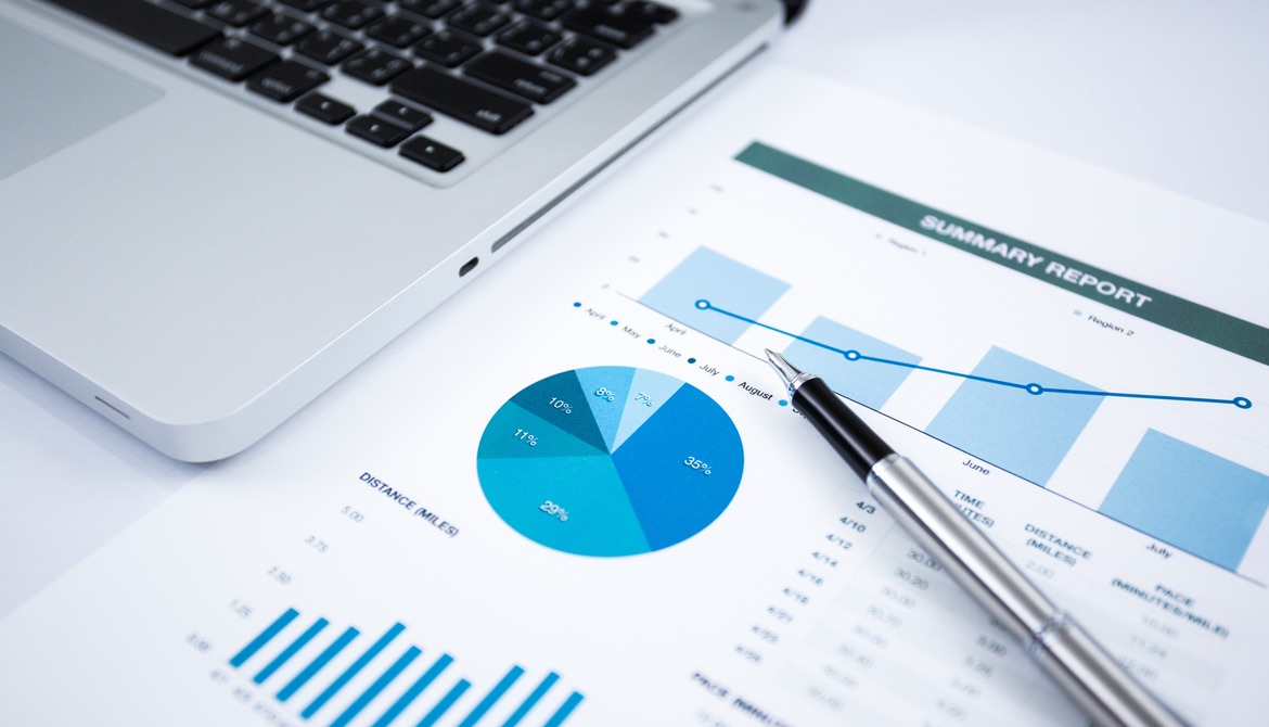 laptop and pen next to financial investment report charts