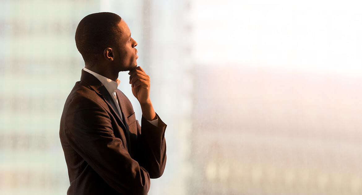 Portrait of pensive African-American businessman standing near window and thinking about decision