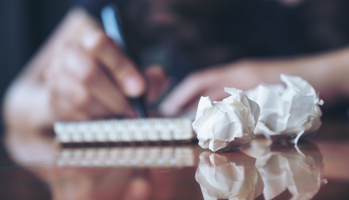 crumpled pieces of paper in front of a person writing pitches in a notebook