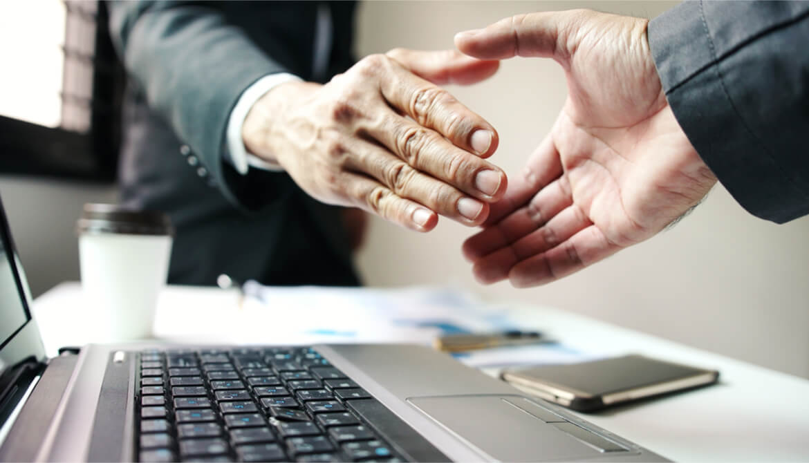 business men shake hands over computer