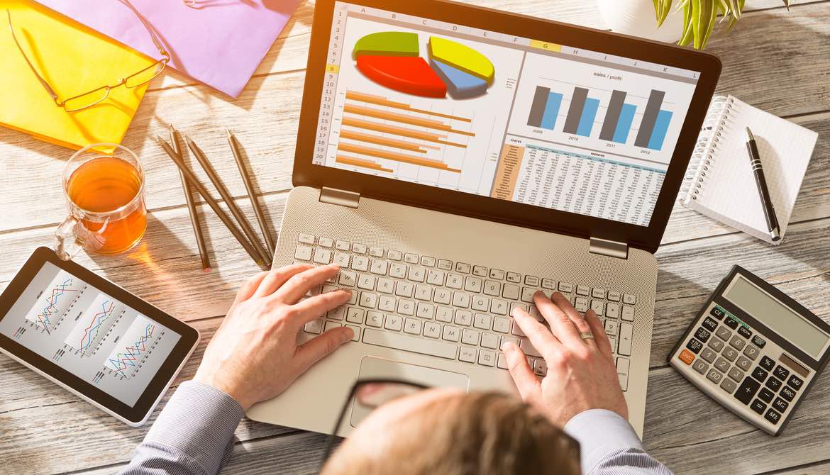 business owner working with accounting software on his laptop, unused calculator and notebook off to the side