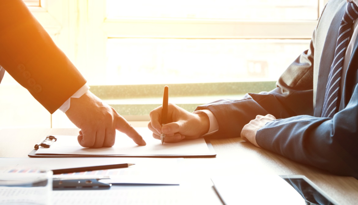 businessman pointing to a contract being signed by another man with a pen