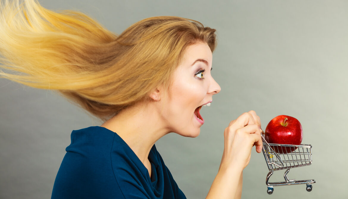 woman holds small shopping cart with an apple in it