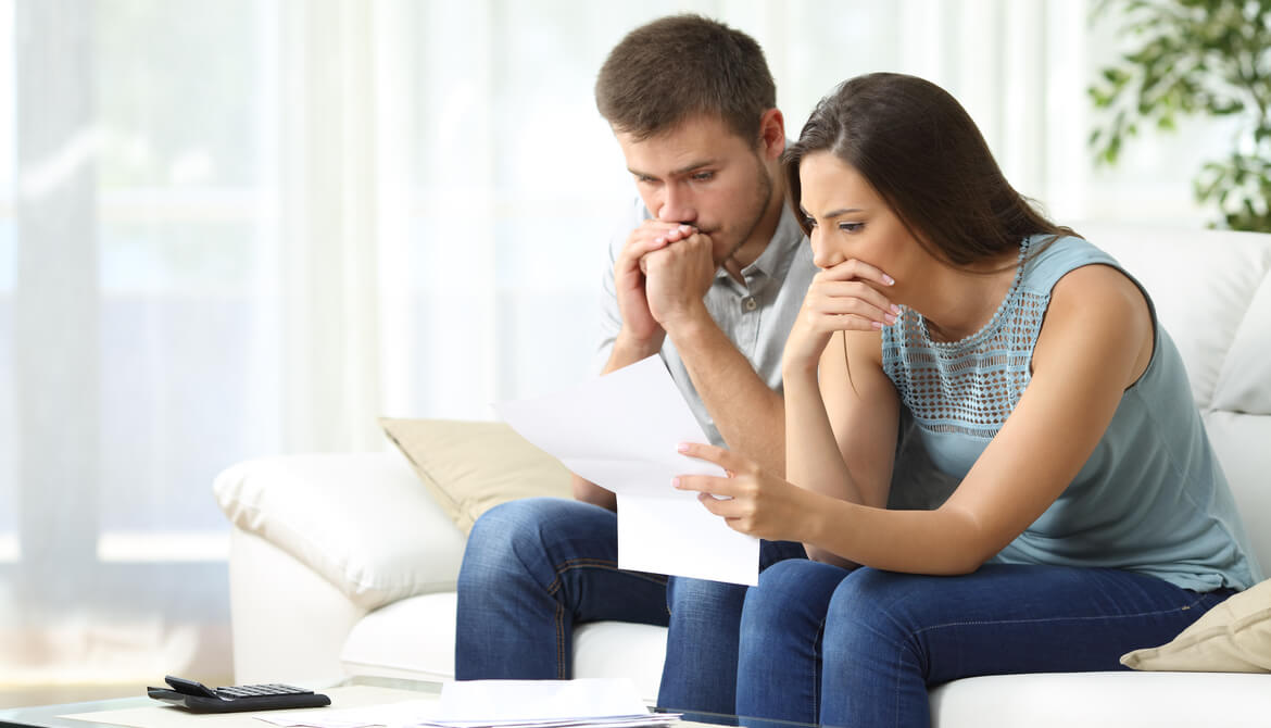 Worried couple reading an important notification in a letter sitting on a couch in the living room at home