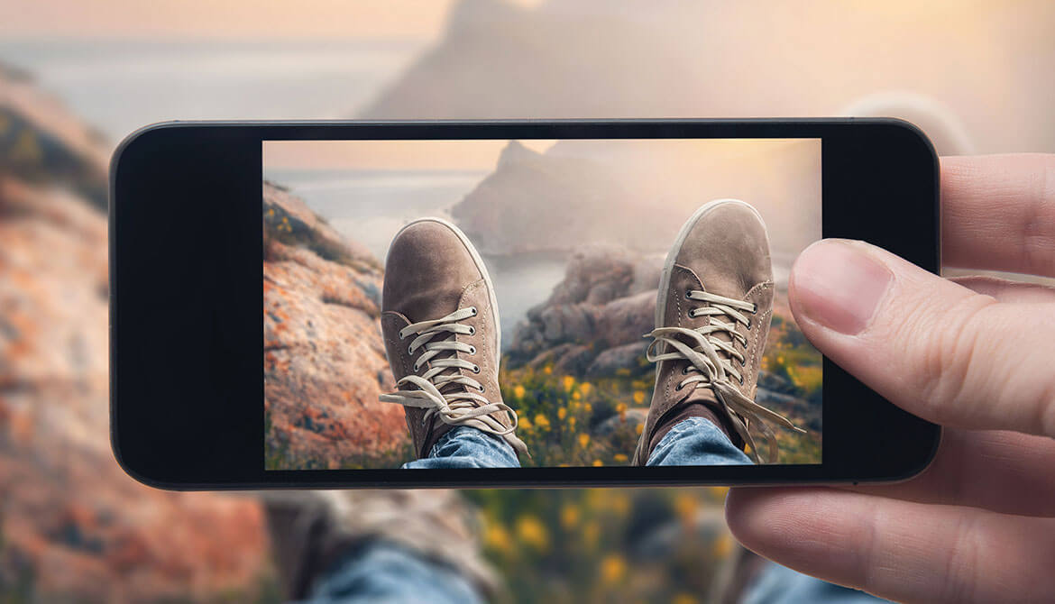 person looking through smartphone camera at their shoes and mountain vista beyond
