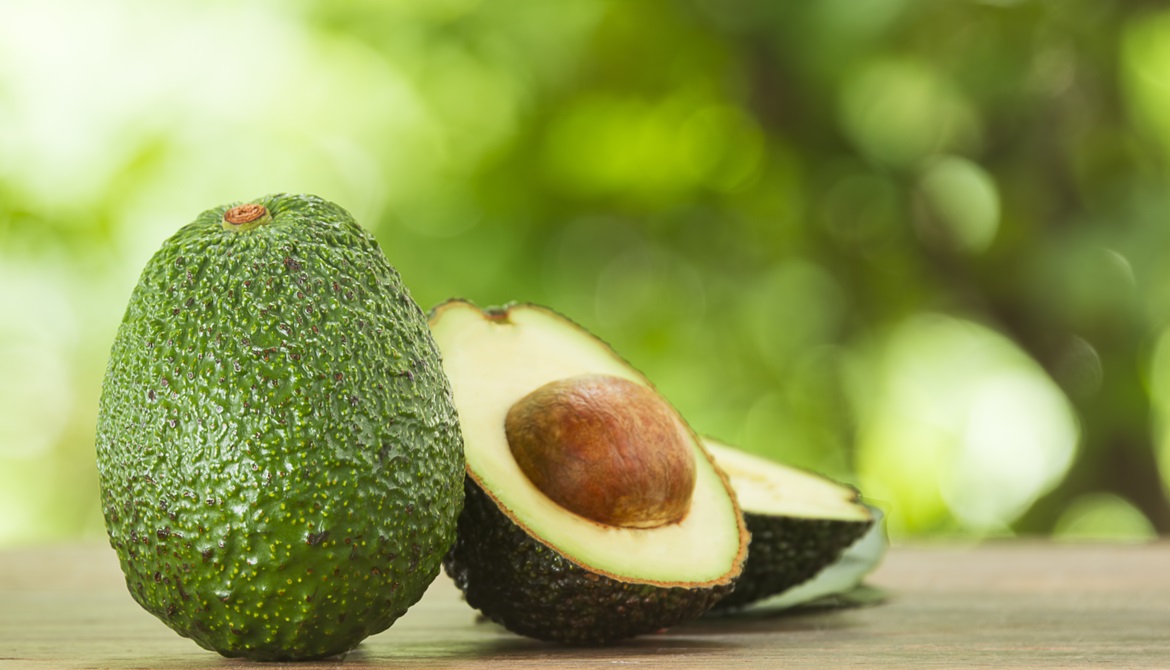 whole unripe avocado next to a ripe avocado sliced in half with pit showing