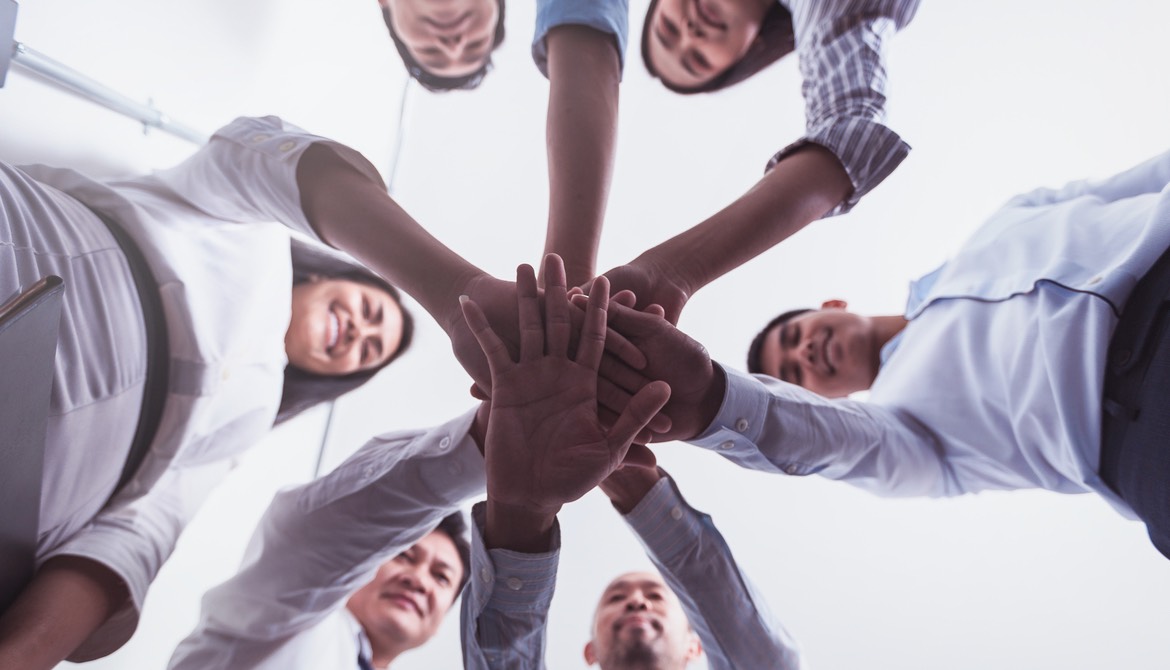 circle of businesspeople putting their hands together in the middle to signify teamwork and support