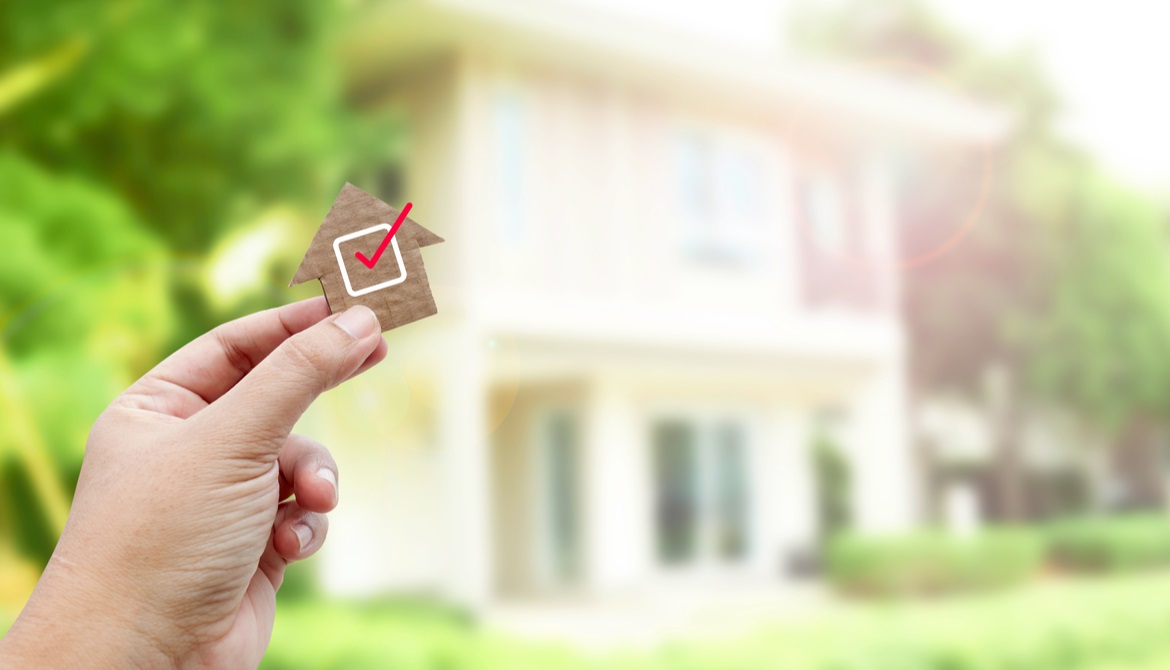 wooden house with red checkmark and a real house in the background