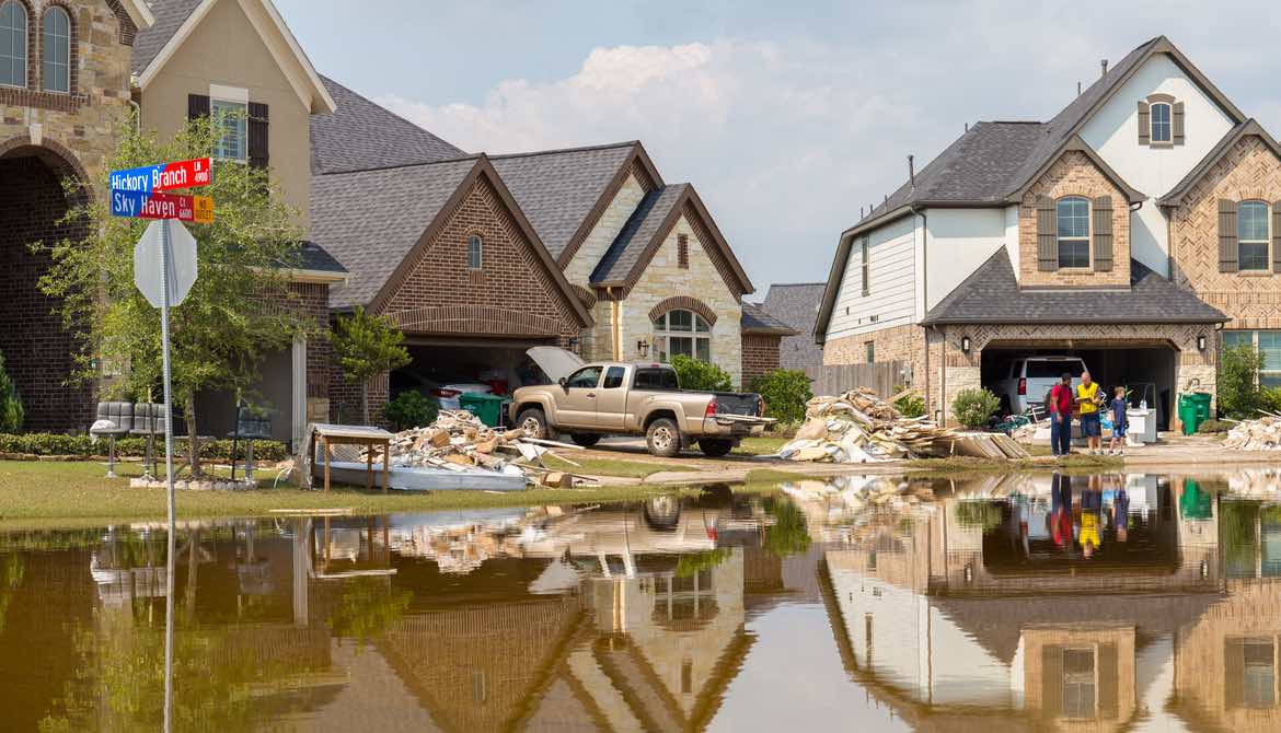 two homes rebuilding with flooding and a man in a yellow emergency worker vest