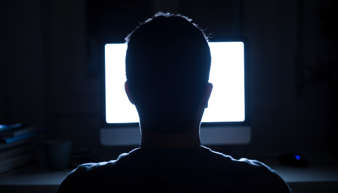 Man sitting in dark in front of bright white computer screen