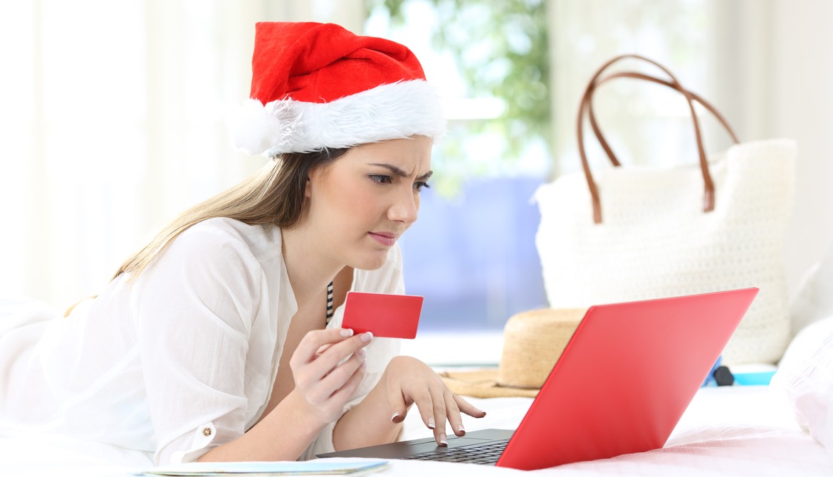confused woman wearing a Santa hat using credit card with a red laptop