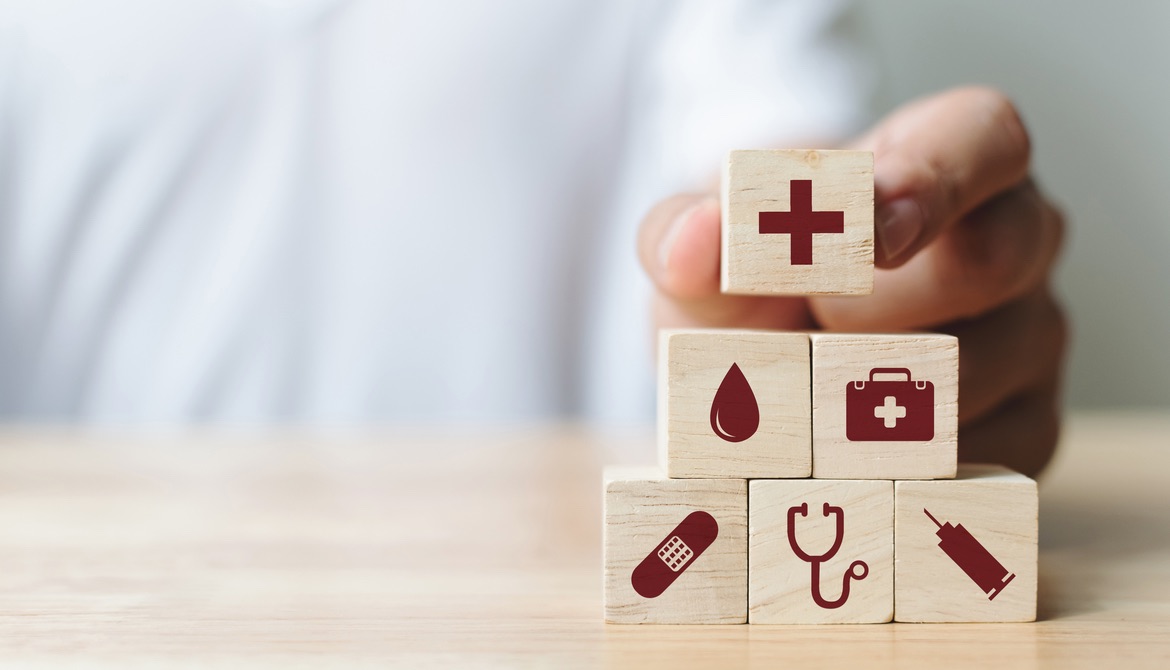 hand stacking wooden blocks with symbols representing health care and insurance
