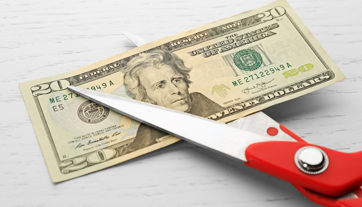 red scissors cutting twenty dollar bill