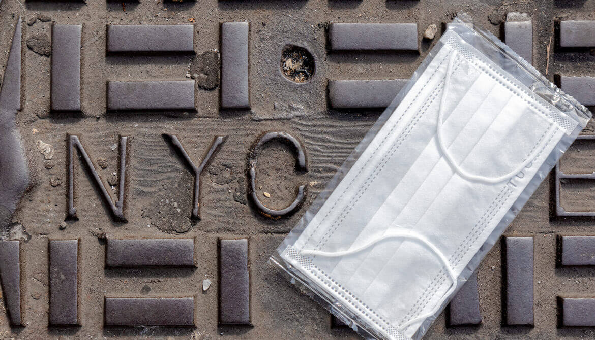 surgical mask on the ground by an NYC stamped in metal