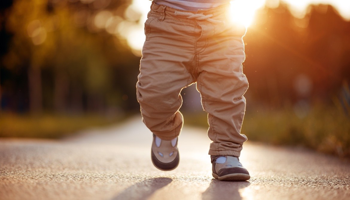 baby walking on sidewalk with sun