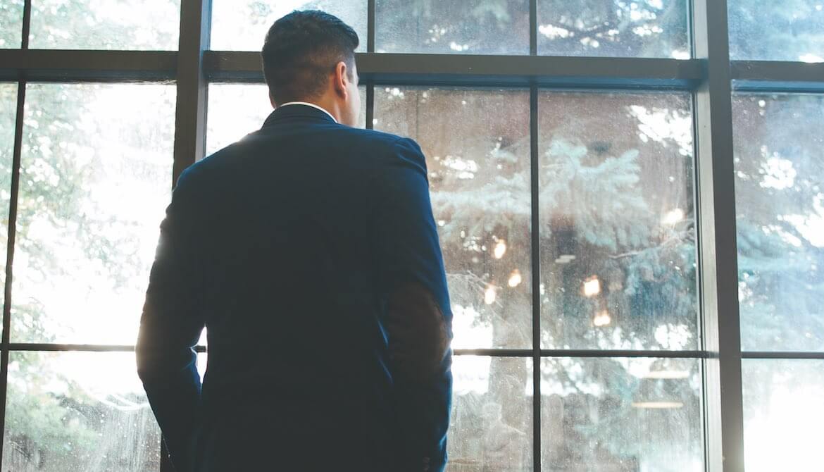 lone businessman in dark suit looks out window to courtyard