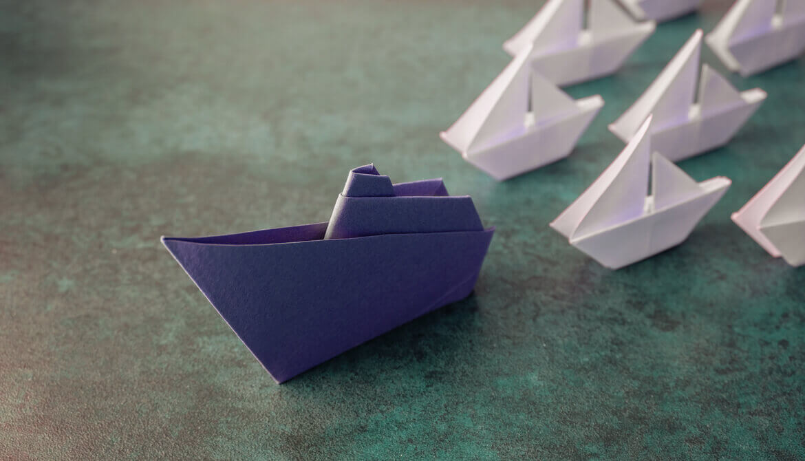 blue origami paper boat leads fleet of smaller white paper boats