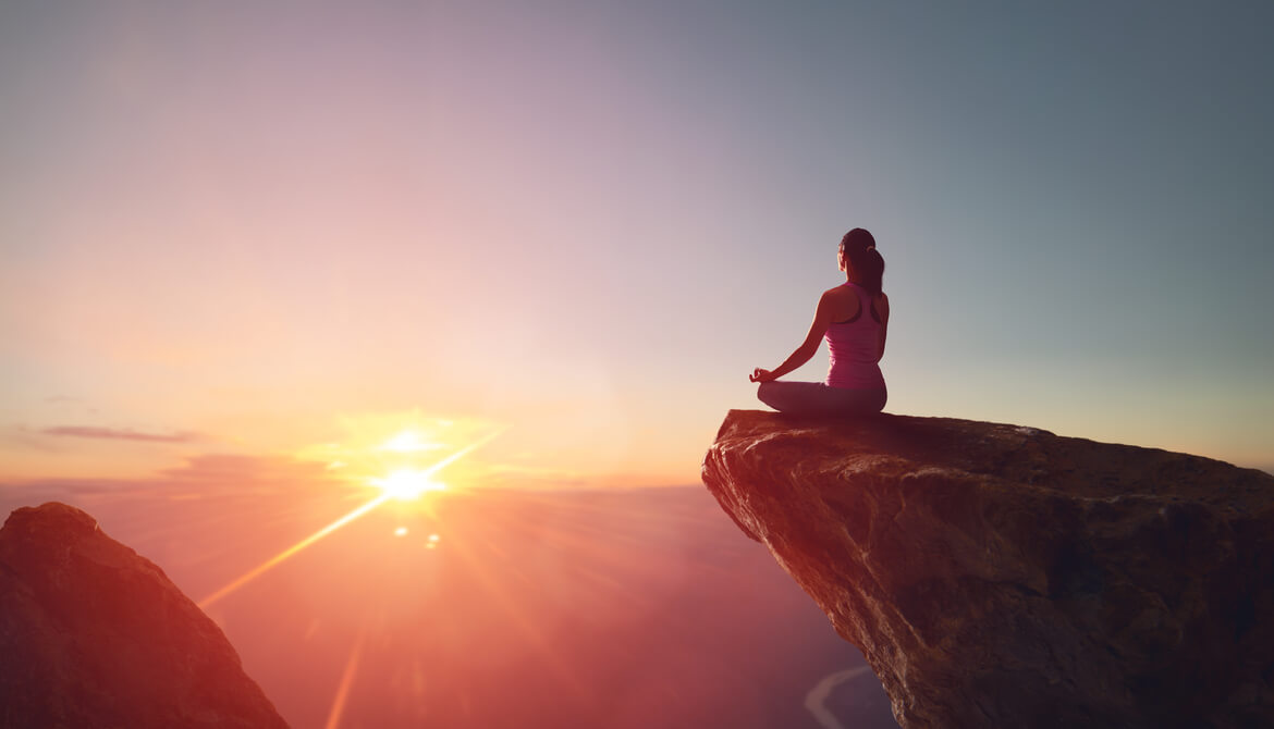 woman meditating on rock outcropping at sunrise