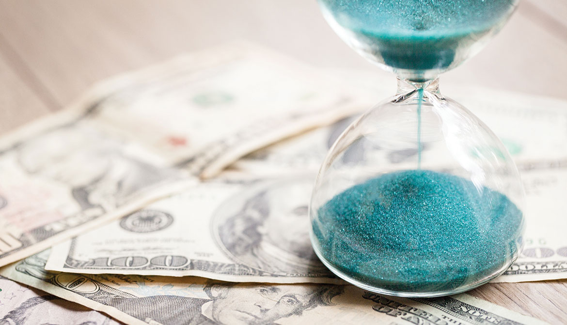 hourglass with blue sand on stop of US bills of various denominations