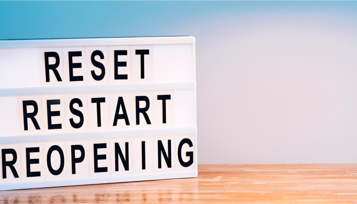 reset restart reopening sign on wooden table in front of blue background