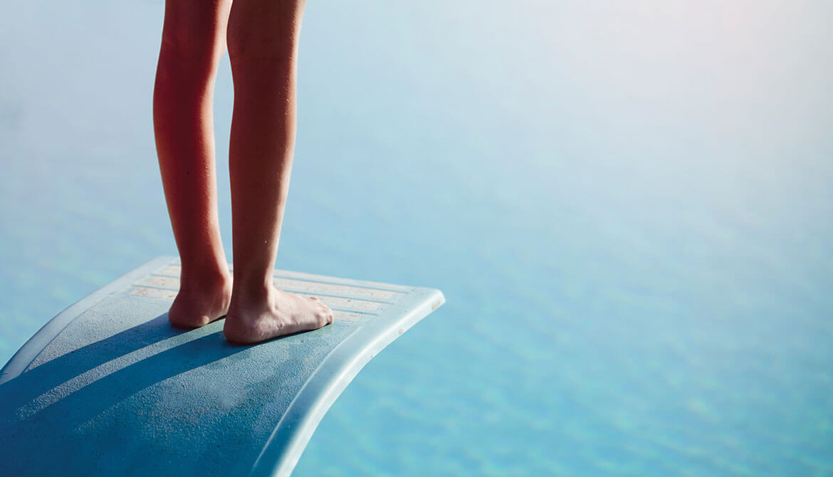 feet of person hesitating near edge of diving board above the water