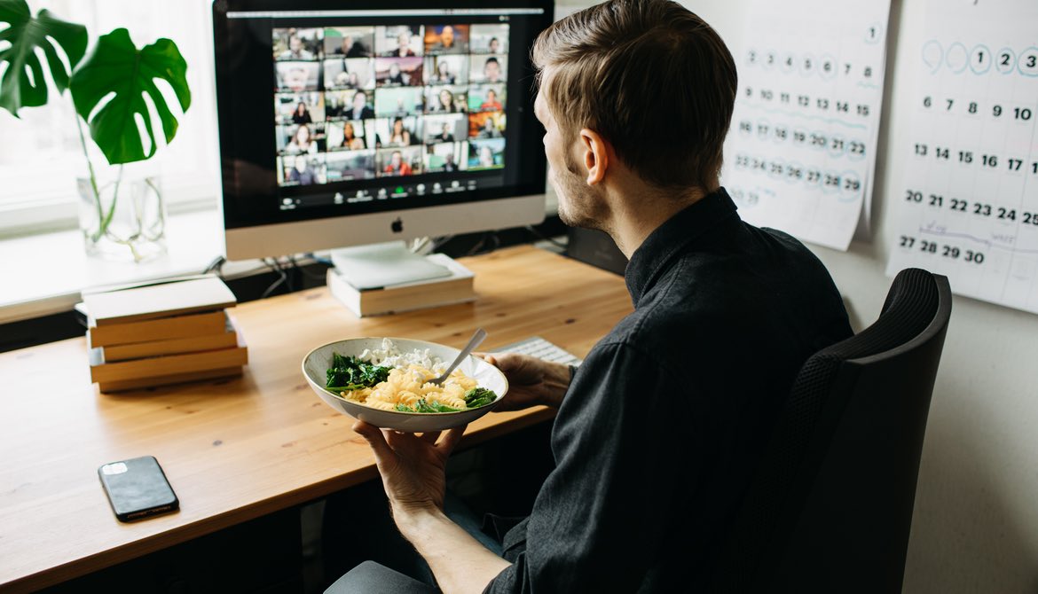 man eating lunch while meeting with colleagues virtually