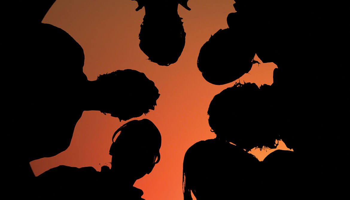 silhouettes of a team of people looking down together in front of an orange sky