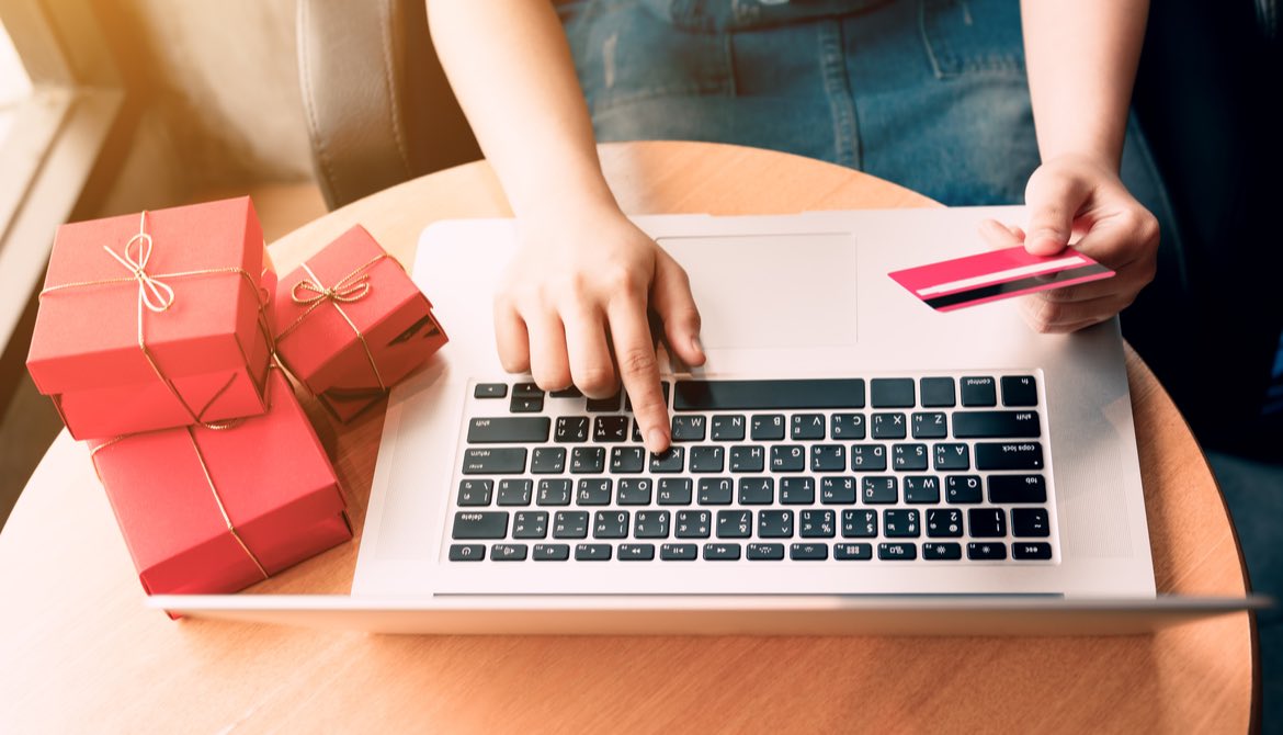 woman with red presents alongside her pays with credit card using laptop