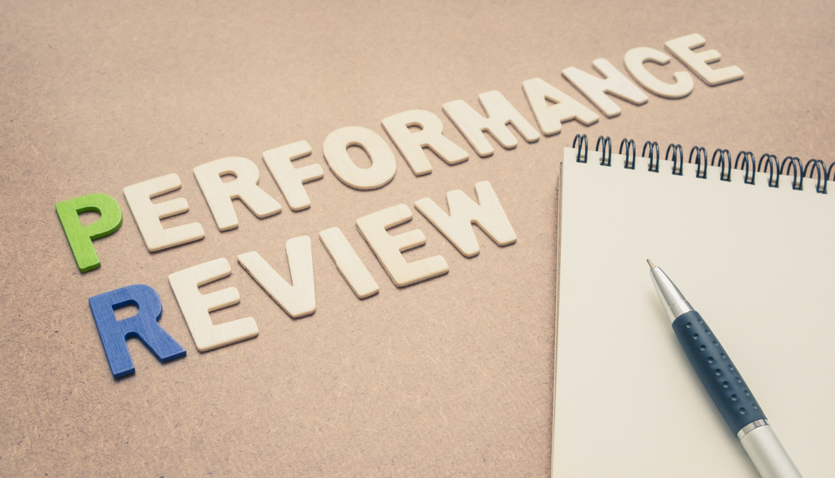 Performance review text with open spiral notebook and pen on brown background